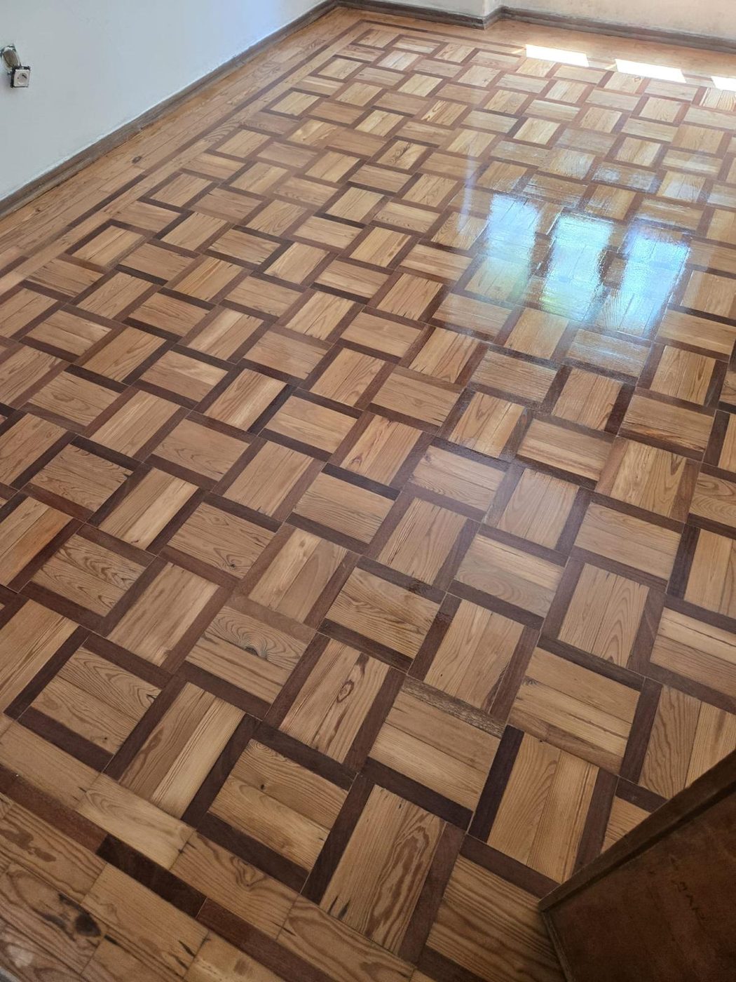 Aplicação da primeira camada de verniz Bona no soalho mosaico, brilho visível na zona já vernizada